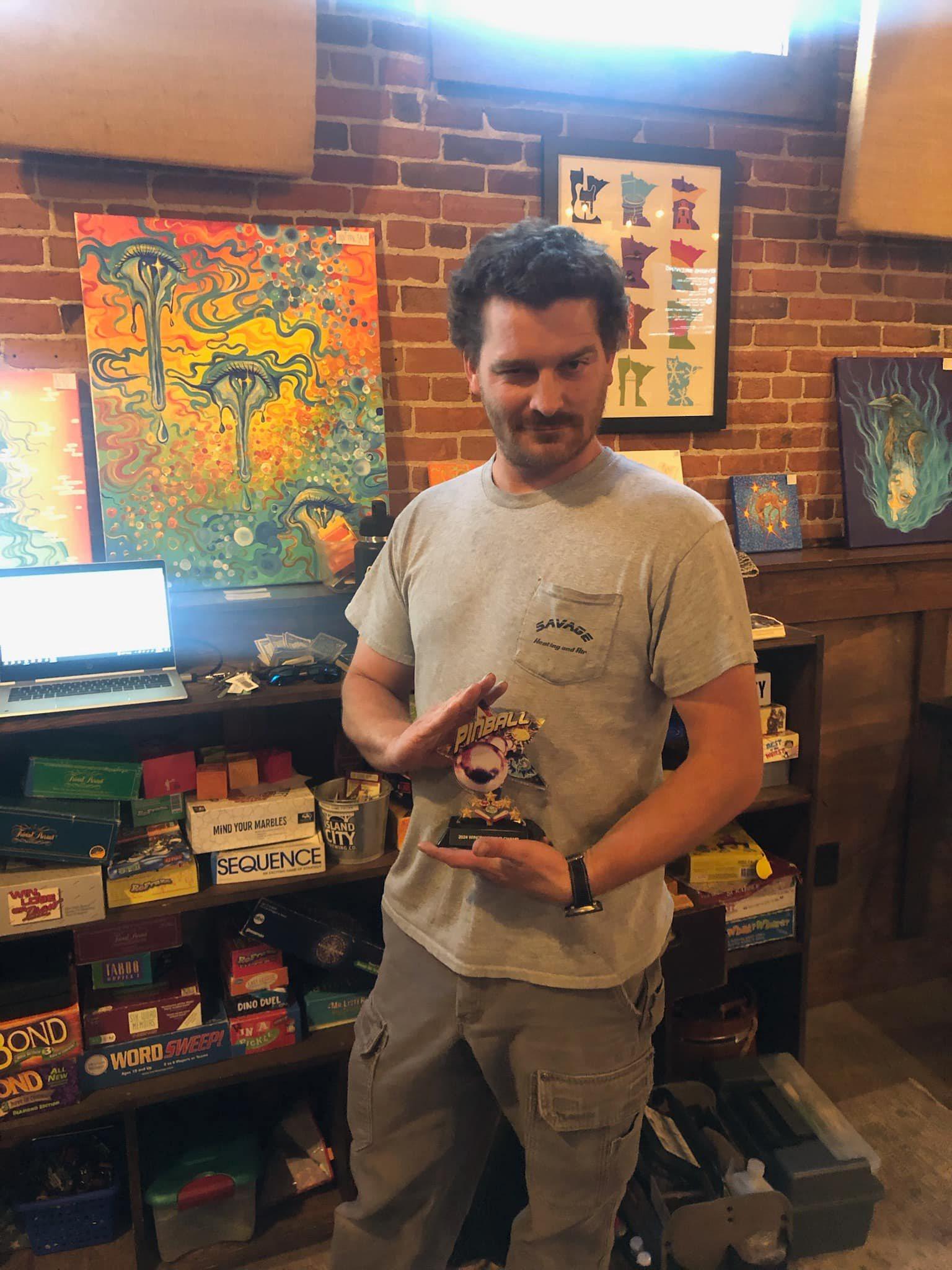 A member of the Bazooka team holding a local pinball tournament trophy
