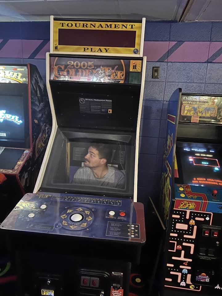 Classic arcade cabinets like Golden Tee and Ms. Pac-Man in a local game room